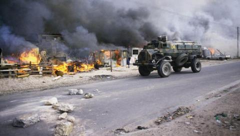 An armoured vehicle patrols past burning houses in the KTC squatter community camp